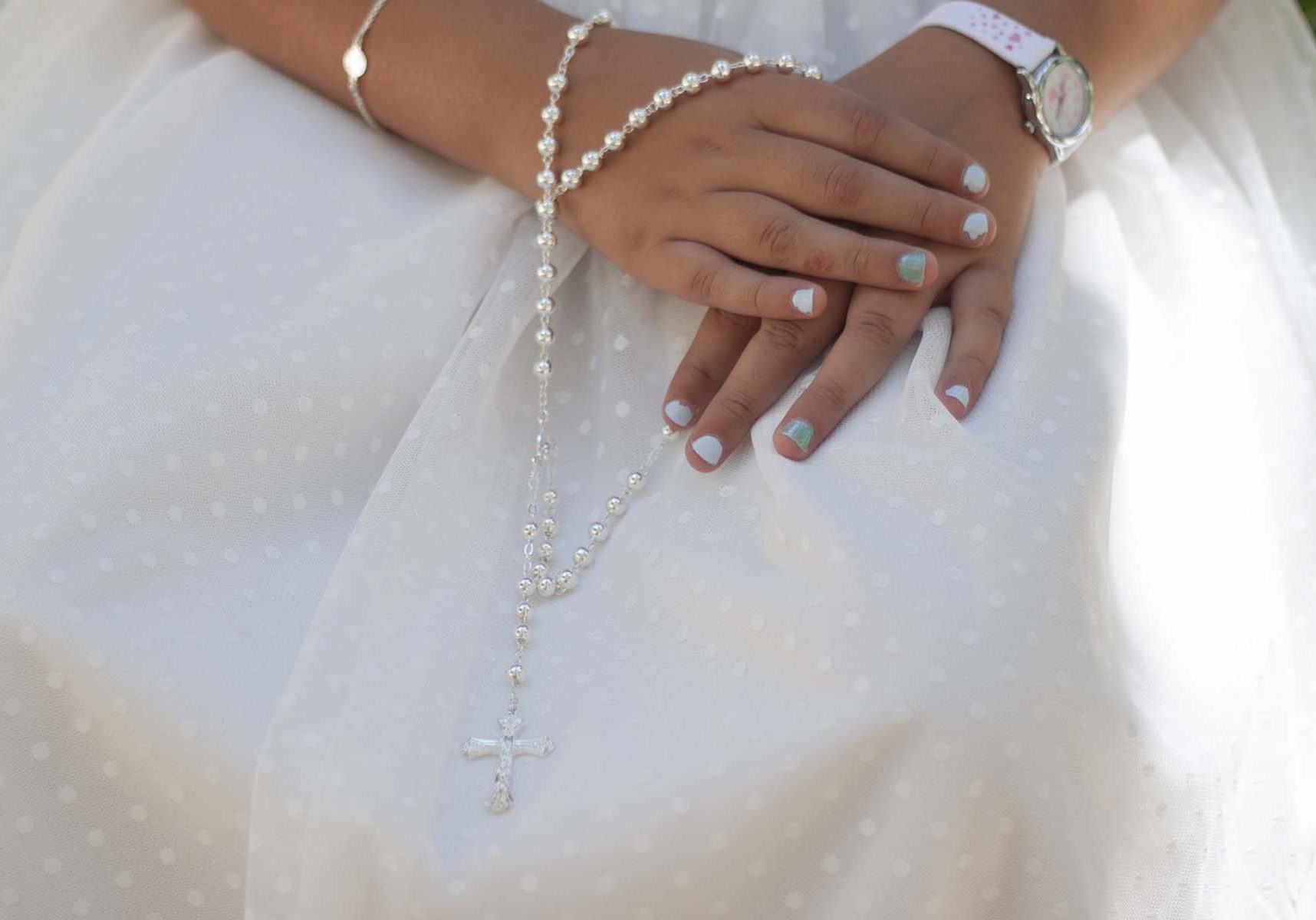 Comm Hands of a girl on a communion dress with a rosary in her hands